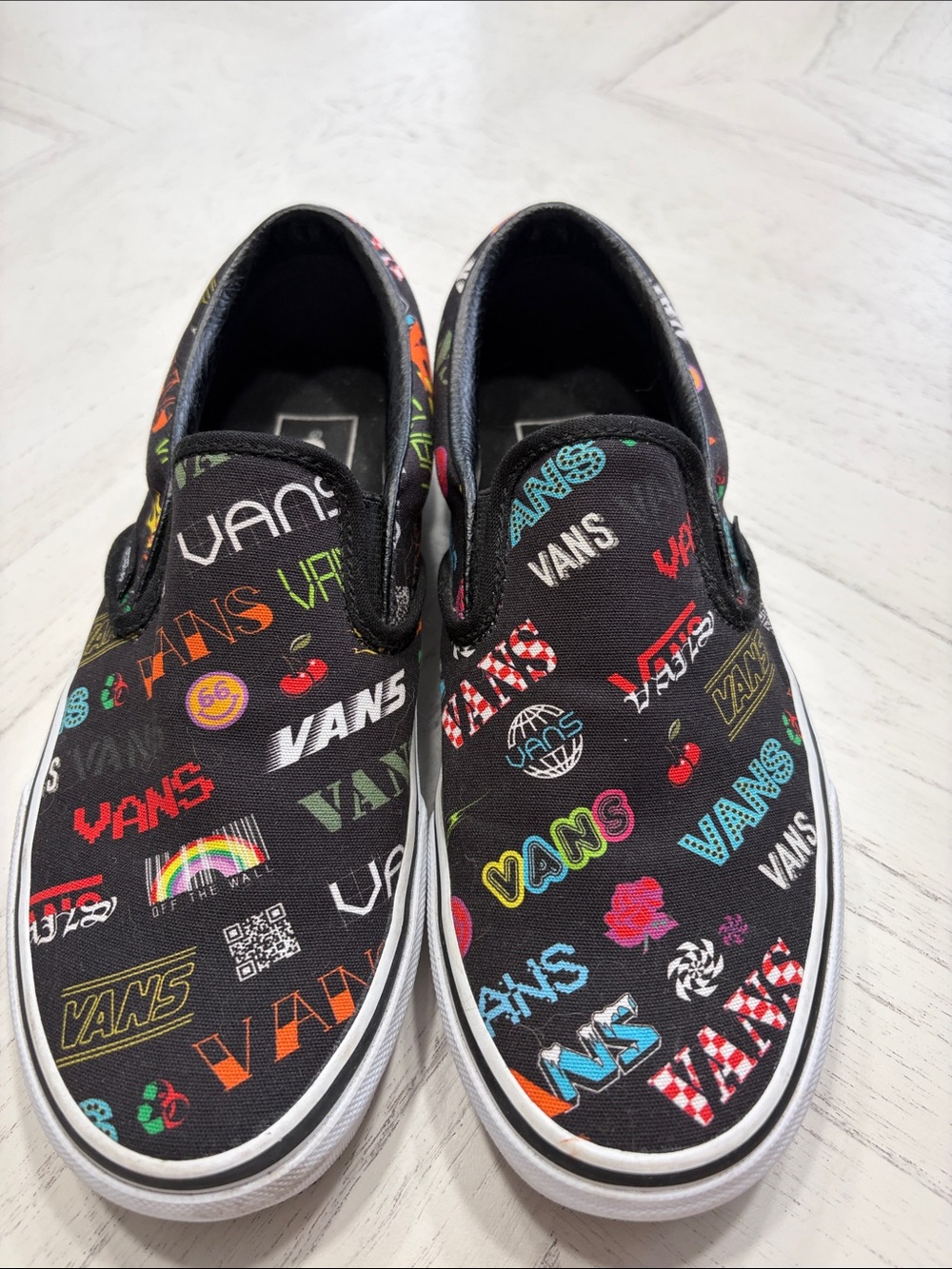 Vans Women’s Slip-On Sneakers in Black with Multi-Color Logo Print